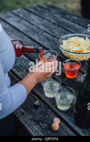 Frau gießt Aperol und macht Spritz Aperitif-Cocktails im Freien auf dem Picknicktisch Stockfoto