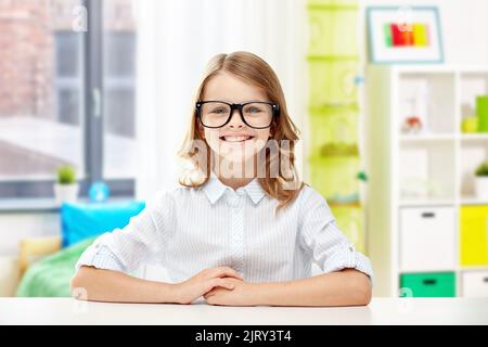 Lächelndes Studentenmädchen in Brille am Tisch sitzend Stockfoto