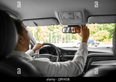 Glücklicher indischer Mann oder Fahrer, der den Spiegel im Auto justiert Stockfoto