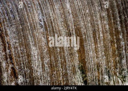 Eine Nahaufnahme eines vom Menschen gemachten Staudamms und Wasserfalls, der an einem sonnigen Wintertag auf dem Land gefunden wurde Stockfoto