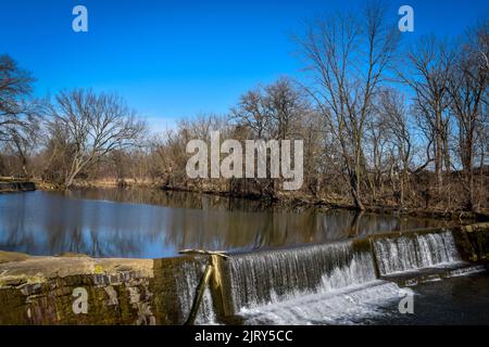 Ein Blick auf einen von Menschen gemachten Damm und Wasserfall, der an einem sonnigen Wintertag auf dem Land gefunden wurde Stockfoto