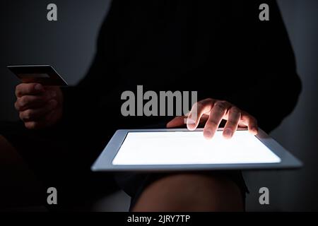 Nur die neueste Technologie wird es tun. Ein nicht identifizierbarer Hacker mit einem Tablet spät in der Nacht. Stockfoto