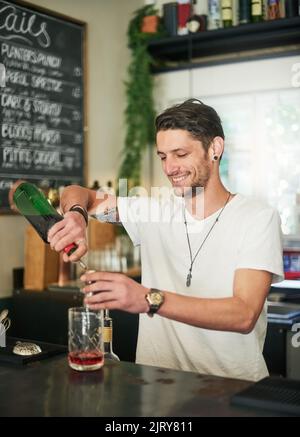 Ein fröhlicher junger Barkeeper mixt einen Cocktail, während er hinter der Bar steht. Stockfoto