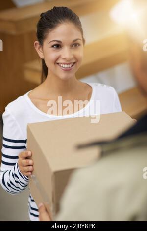 Eine junge Frau, die ihr Paket vom Kurier erhält, hinterlässt einen weiteren zufriedenen Kunden mit einem großen Lächeln. Stockfoto