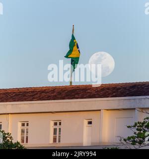 Vollmond steigt neben der Flagge brasiliens auf dem Dach der copacabana Festung in rio de janeiro Brasilien. Stockfoto