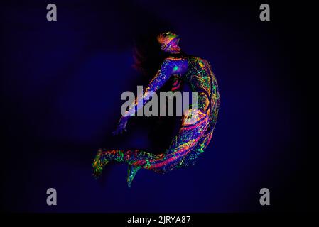 Schönheit leuchtet im Dunkeln am hellsten. Ganzkörperaufnahme einer jungen Frau, die mit Neonfarbe auf ihrem Gesicht posiert. Stockfoto