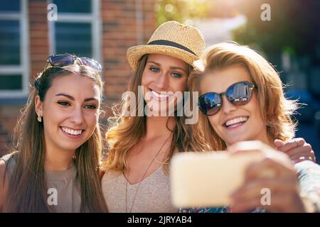 Es gibt immer Zeit für ein Selfie. Drei junge Freundinnen nehmen Selfies im Freien auf. Stockfoto