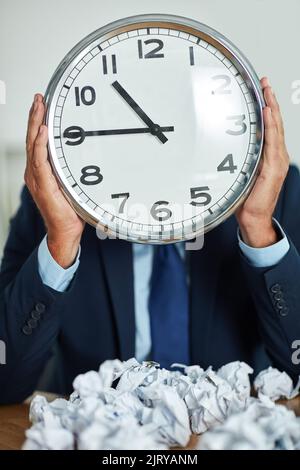 Die Zeit läuft aus. Ein nicht erkennbarer Geschäftsmann hält eine große Uhr vor seinem Gesicht. Stockfoto