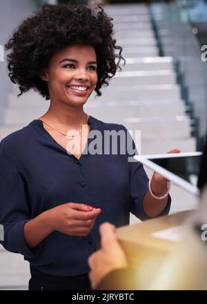 Eine glückliche Geschäftsfrau, die ein Paket von einem Kurier im Büro annimmt. Stockfoto