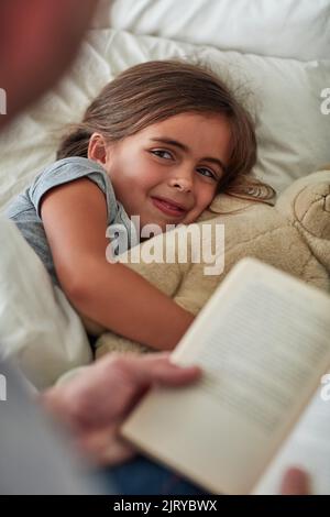 Sie kann nicht schlafen, ohne zuerst ihre Lieblingsgeschichte zu lesen. Ein kleines Mädchen liegt im Bett, während ihr Vater ihr eine Geschichte vorliest. Stockfoto