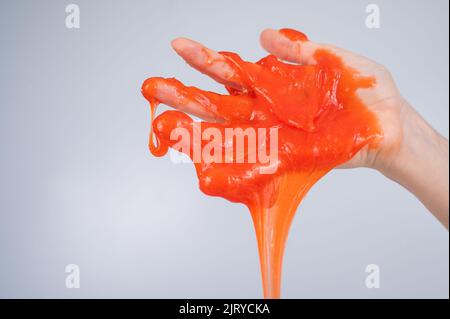 Roter Schleim, der aus der Hand einer Frau auf einem weißen Hintergrund herabfließt. Stockfoto