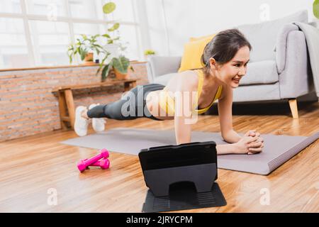 Asiatische schöne Frau im Sport tragen Bewegung und trainieren zu Hause durch folgende Trainer in VDO-Konferenz auf Tablet Stockfoto