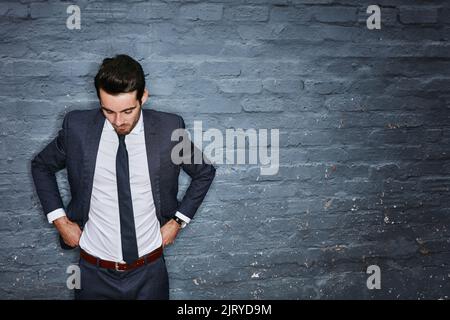 Ein Geschäftsmann, der seine Hose an eine graue Wand anpasst. Stockfoto