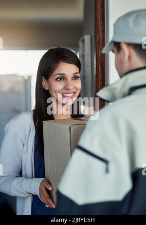 Ein schneller und freundlicher Service bringt sie zum Lächeln. Eine junge Frau erhält ihr Paket vom Kurier. Stockfoto