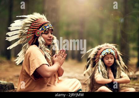 In Kontakt mit ihren Vorfahren. Eine junge Frau und ihre Tochter meditieren, während sie im Wald Dressup spielen. Stockfoto