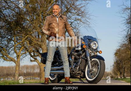 Mann mittleren Alters mit Lederjacke, der vor seinem Motorrad steht und eine Sonnenbrille in der Hand hält, Karlsruhe, Deutschland Stockfoto