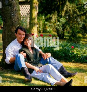 Junges Paar, das unter einem Baum auf einer Wiese sitzt Stockfoto