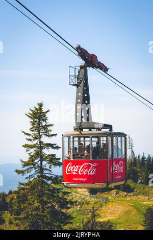 Eine Gruppe von Menschen in einer Seilbahn mit Coca-Cola-Aufdruck darauf Stockfoto