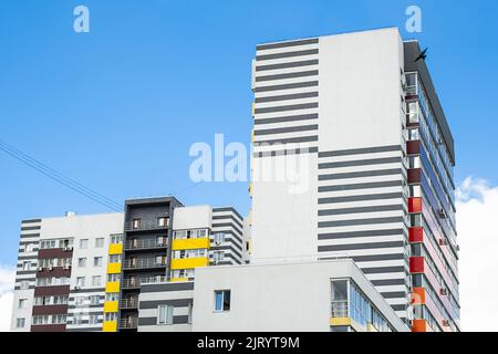 Mehrfarbige Wohnhochhäuser vor blauem Himmel. Städtischer Immobilienhintergrund. Stockfoto