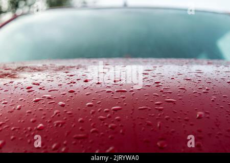 Spritzer und Wassertropfen auf einer roten Autooberfläche bilden einen schönen Hintergrund mit Texturmuster. Stockfoto