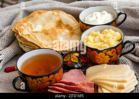 Frühstück im Bett für Ihre Liebsten, Pfannkuchen mit saurer Rahm, Käse und Fleisch, Maisbrei und eine Tasse frisch gebrühten Tee. Guten Morgen! Stockfoto