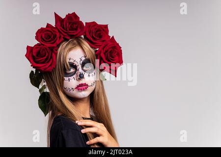 Teenager-Mädchen mit coolen Schädel Make-up mit Rosen auf dem Kopf Blick auf die Kamera im Studio Stockfoto