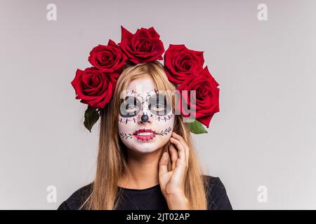 Teenager-Mädchen mit coolen Schädel Make-up mit Rosen auf dem Kopf Blick auf die Kamera im Studio Stockfoto