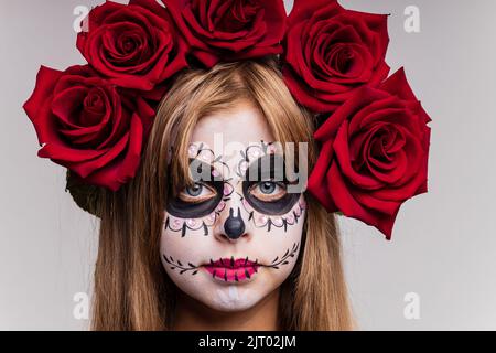 Teenager-Mädchen mit coolen Schädel Make-up mit Rosen auf dem Kopf Blick auf die Kamera im Studio Stockfoto