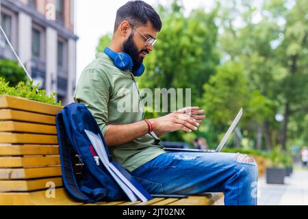 ein indischer Mann startet einen Geschäftsmann, der im Park sitzt und an einem Laptop arbeitet Stockfoto