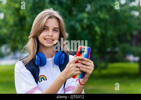 kaukasisches Mädchen Teenager Student verwenden Smartphone mit Regenbogengehäuse im Freien im Stadtpark Stockfoto