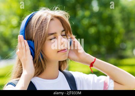 kaukasisches Mädchen Teenager Student hören die Musik Stereo Lieblingslied in Kopfhörern im Freien im Stadtpark Stockfoto