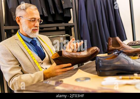 Ein älterer Schuhmacher, der in einer Werkstatt handgefertigte männliche Schuhe und Gürtel zeigt Stockfoto