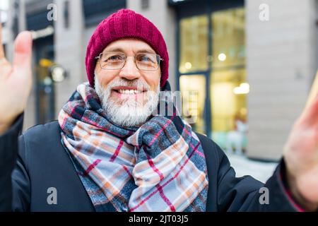 Glücklich gut aussehender reifer Mann, der einen Videoanruf mit seiner Familie auf dem Wintermarkt in der Stadt macht Stockfoto