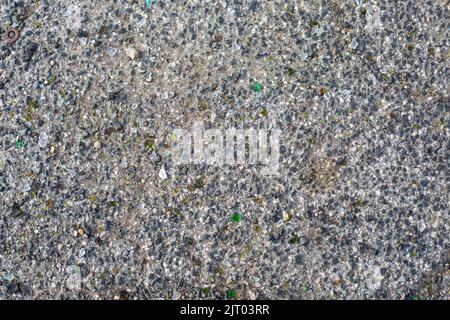 Hintergrund von altem Asphalt. Graue Straßenoberfläche mit kleinen Felsen und grünen Stücken aus gebrochenem Glas. Stockfoto