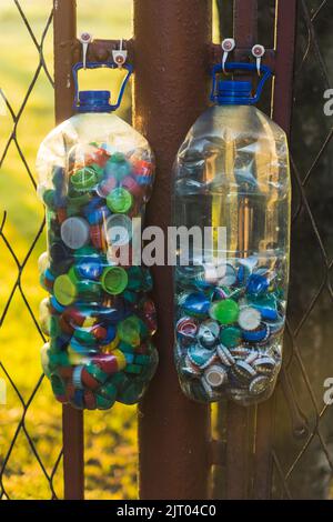 Wasserbehälter aus Kunststoff, gefüllt mit Plastikflaschen, die auf dem Land am Metallzaun hängen. Recycling. Nahaufnahme der vertikalen Aufnahme. Hochwertige Fotos Stockfoto