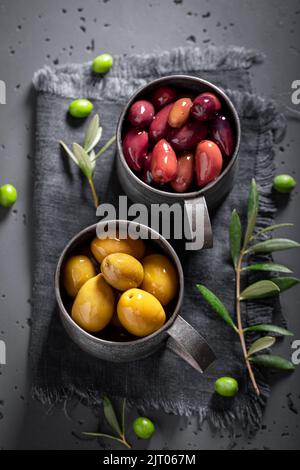 Grüne und schwarze Oliven in einer Schüssel mit einem Olivenzweig. Produkte aus Oliven. Stockfoto