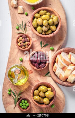 Leckere Oliven und natives Olivenöl extra mit Brot serviert. Set aus grünen und schwarzen Oliven in Holzschüsseln. Stockfoto