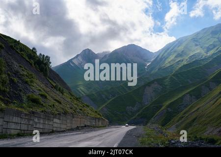 Straße im Hochland mit riesigen felsigen Bergen und Hängen in Dunst bei sonnigem Wetter gebaut Stockfoto