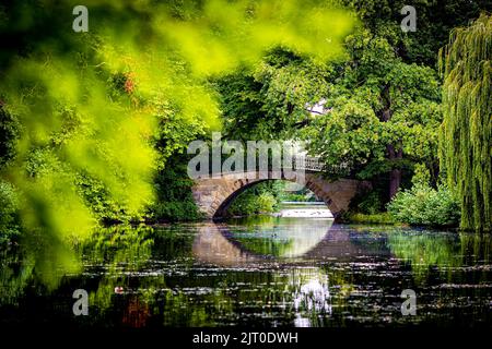 Hannover, Deutschland. 27. August 2022. Eine Brücke im Georgengarten bei den Herrenhauser Gärten spiegelt sich bei bewölktem Wetter auf der Wasseroberfläche eines Teiches. Quelle: Moritz Frankenberg/dpa/Alamy Live News Stockfoto