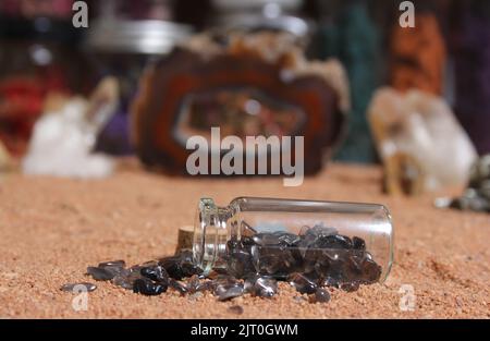 Flasche Chakra-Steine auf rotem Sand mit agatisierter Koralle im Hintergrund Stockfoto