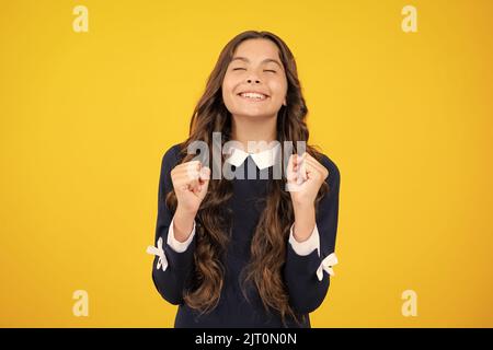 Froh Teenager-Mädchen kreuzt die Finger, schließt die Augen mit Vergnügen, erwarten hören gute Nachrichten, isolierten gelben Hintergrund. Glückliches Kind freut sich, dass seine Stockfoto