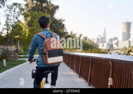 Rückansicht eines asiatischen jungen erwachsenen Mannes, der im Stadtpark Fahrrad reitet Stockfoto