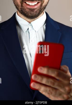 Ein Mann in einem Anzug, der sein rotes Telefon hält und lächelt Stockfoto