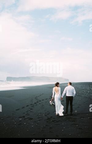 Braut und Bräutigam gehen entlang Vik Strand in Island Stockfoto