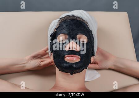 Verjüngungsverfahren für das Gesicht. Schwarze Stoffmaske auf dem Gesicht der Frau. Stockfoto