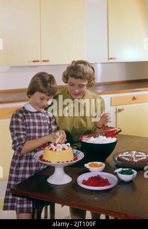 Backen Sie einen Kuchen in der 1950s. Eine Mutter und ihre Tochter in der Küche, die den Kuchen mit Sahnehahne fertig machen. Schweden 1958 Conard Ref. BV89-11 Stockfoto