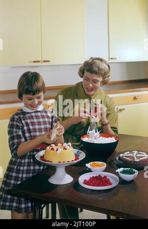 Backen Sie einen Kuchen in der 1950s. Eine Mutter und ihre Tochter in der Küche, die den Kuchen mit Sahnehahne fertig machen. Schweden 1958 Conard Ref. BV89-12 Stockfoto