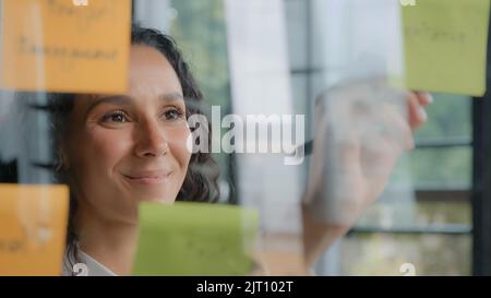 Junge positive hispanische Frau Büroangestellte schreibt Projektaufgaben auf Haftnotizen organisiert Arbeitspläne Strategie erfolgreiche Geschäftsfrau entwickelt Plan Stockfoto