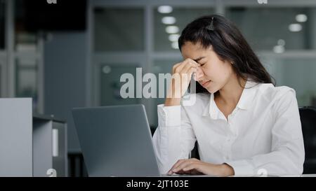 Junge gestresste müde überarbeitete weibliche Büroangestellte, die an einem Laptop mit Augenermüdungsmassagen arbeitet, fühlt sich Nasenrücken angespannt Kopfschmerzen an Stockfoto