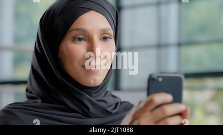 Nahaufnahme positive arabische Frau in Hijab hält Telefon Ordnung im Online-Shop freundlich lächelnde muslimische weibliche Berater reagiert auf Client im Web Stockfoto